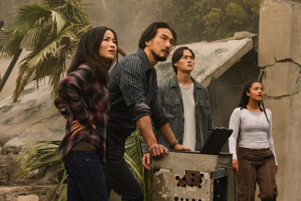 Cate, Hiroshi, Kentaro Randa, and May are standing in front of a Suzuki device while looking up at something in the distance in Monarch: Legacy of Monsters Season 2.